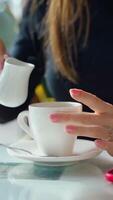 Woman pouring milk into coffee cup on the table. Hands of a young lady adding hot milk to coffee in a cafe. Close-up. Slow motion. Vertical video