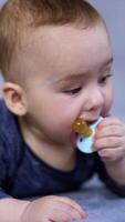 Cute adorable baby boy dealing with a pacifier. Beautiful infant child chewing the soother and looking aside. Close up. Grey blurred backdrop. Vertical video
