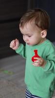One year Caucasian toddler just started walking. Kid with a toy in hand turns from camera and walks slowly away. Vertical video