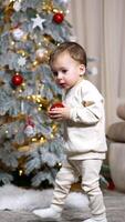 Adorable baby has a red ball from Christmas tree in his hands. Kid walks away with a toy approaching camera. Vertical video