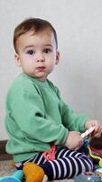 Cute child distracted from his game with a toy. Baby boy plays with toy and then looks at camera intently. Vertical video