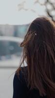 Back view of a woman walking in the autumn park with long dark hair turning back to the camera. Selective focus used in Vertical video