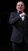 Man is speaking in the light of the floodlights standing on stage to the camera. Actor, artist on performance. Activ gestures with hands. Vertical video