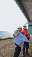 Technicians installing solar panel. Men engineers in helmets connecting photovoltaic panels on the solar farm outdoors. Vertical video