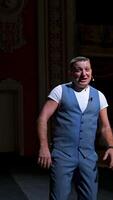 Showman entertains the audience under the light, front view. Big stage. Funny performer speaks to the camera. Active gestures on a stage. Vertical video