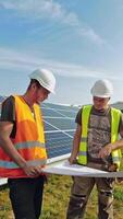 Installation of solar panels. Workers discussing the blueprint of new sunny cells. Engineers talking about photovoltaic panels on solar farm. Vertical video