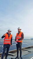 Solar generation technologies. Engineers standing on a flat roof with many solar panels. Workers in protective outfit and hard hats are talking on a modern solar farm. Vertical video