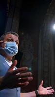 Actor in elegant suit and medical mask. Actor in protective facial mask standing on stage of a theater. Coronavirus and pandemic concept. Vertical video