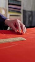 Seamstress making pattern on fabric. Dressmaker working at desk pointing with pattern Vertical video
