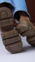 Convenient brown suede sneakers on massive soles and same color laces. Model wearing blue jeans sits on the chair posing in her shoes in front of camera. Close up. Vertical video