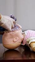 Demonstration of cpr on a baby model. Instructor in medical gloves showing the right breathing exercise on a dummy in training center. Side view. Vertical video