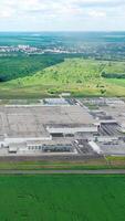 Industrial complex among fields. Panoramic view of a large manufacturing in green natural environment. Aerial view. Motion back. Vertical video