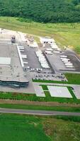 Roofs of a huge industrial factory in green nature. Flight over contemporary complex with parking zones on field. Aerial view. Vertical video