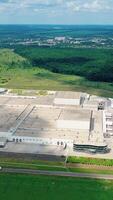 Roofs of a huge industrial plant at sunlight. Modern factory of white building with places for cars and trucks on green field. Vertical video