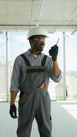 African american builder use walkie talkie on a construction site indoors. Vertical video