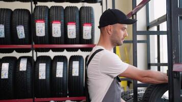 Car mechanic in overalls pulls a tire for customer in the warehouse video