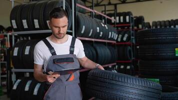 male salesman in auto shop making notes, checking the document and examining characteristics, looking at rack with auto rims video