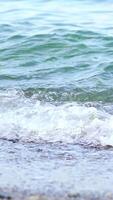 Close up of water edge and sand. Close up view of blue sea water waves with bubbles on sand beach. Vertical video