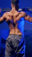 Man training on horizontal bar in gym. Back view portrait of young bodybuilder doing pull ups on the horizontal bar indoors. Vertical video