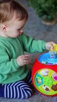 Peaceful one year old child playing with a toy on the floor. Baby boy turns the toy and presses buttons on it. Vertical video