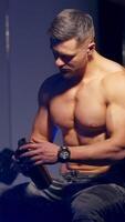 Muscular Man Resting After Exercise. Muscular caucasian man drinking protein powder from shaker after exercise. Vertical video