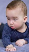 Lovely Caucasian child looks sideways with surprise. Astonished little kid watching something with an open mouth. Close up. Grey backdrop. Vertical video