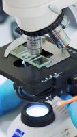 Laboratory examination of blood. Close up of female scientist in uniform working with microscope in the laboratory. Vertical video