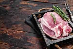 Ready for cooking raw pork chop steaks in a wooden tray with rosemary. Wooden background. Top view. Copy space photo