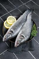 Fresh Raw Sea Bass fish with lemon and thyme. Black background. Top view photo