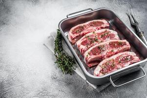 Marinated Raw meat of lamb mutton saddle in steel tray with thyme, spices and olive oil. White background. Top view. Copy space photo