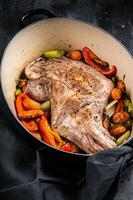 Roasted lamb mutton shoulder meat in a baking dish with vegetables. Black background. Top view photo