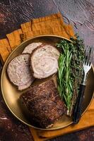 Slices of roasted stuffed pork meat roulade on a plate with rosemary and thyme. Dark background. Top view photo