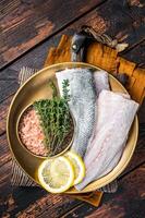 Uncooked Raw Sea Bass fillets, Seabass fish with thyme, pink salt and lemon. Dark background. Top view photo