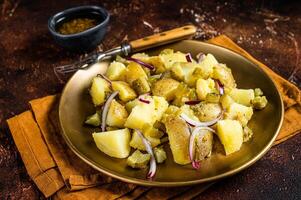Warm Potato salad with red onion, capers, greens in a plate. Dark background. Top view photo