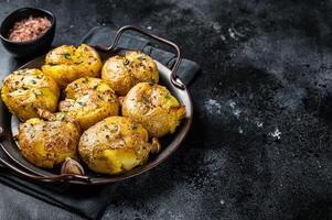 Broken potatoes baked in oil with herbs. Black background. Top view. Copy space photo