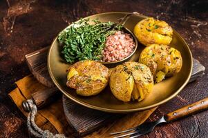 Crushed, smashed potatoes baked with rosemary and thyme on plate. Dark background. Top view photo