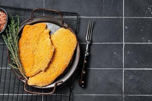 Homemade raw breaded German Weiner Schnitzel. Black background. Top view. Copy space photo