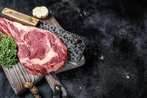 Dry aged Tomahawk rib eye steak, raw beef meat on butcher table. Black background. Top view. Copy space photo