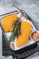 Cooking raw chicken schnitzel in breadcrumbs, uncooked meat steak. Gray background. Top view photo