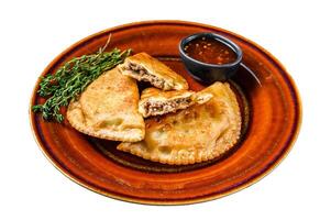 Fried empanadas with minced beef meat served on a plate with chili sauce. Isolated on white background, top view. photo