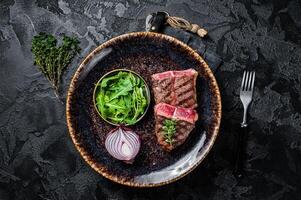 Grilled Oyster Top Blade beef meat steak on a plate with salad. Black background. Top View photo