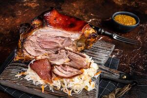 Schweinshaxe Roasted Pork Ham Hock, knuckle with Sauerkraut served on a wooden board. Dark background. Top view photo