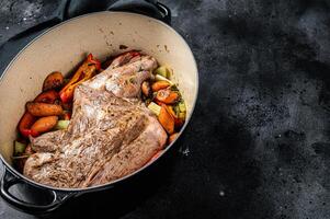 Roasted lamb mutton shoulder meat in a baking dish with vegetables. Black background. Top view. Copy space photo