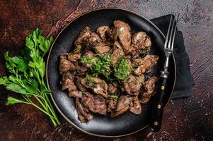 Fried chicken liver with onions and parsley in a plate. Dark background. Top view photo