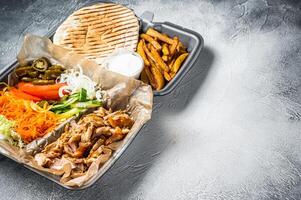 Doner kebab Shawarma on a plate with french fries and salad in box to go, take away. White background. Top view. Copy space photo