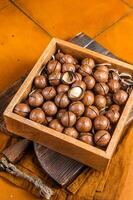 Macadamia natural nuts in a box. Orange background. Top view photo