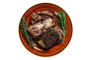 Grilled short beef ribs with thyme on a rustic plate. Isolated on white background. photo