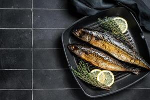 Grilled mackerel fish with lemon, herbs and spices in a skillet. Black background. Top view. Copy space photo