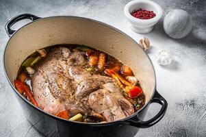 Braised lamb mutton shoulder in a baking dish with vegetables in red wine. White background. Top view photo