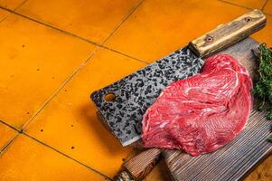 Piece of Raw beef meat for stew with herbs on butcher cutting board. Orange background. Top view. Copy space photo